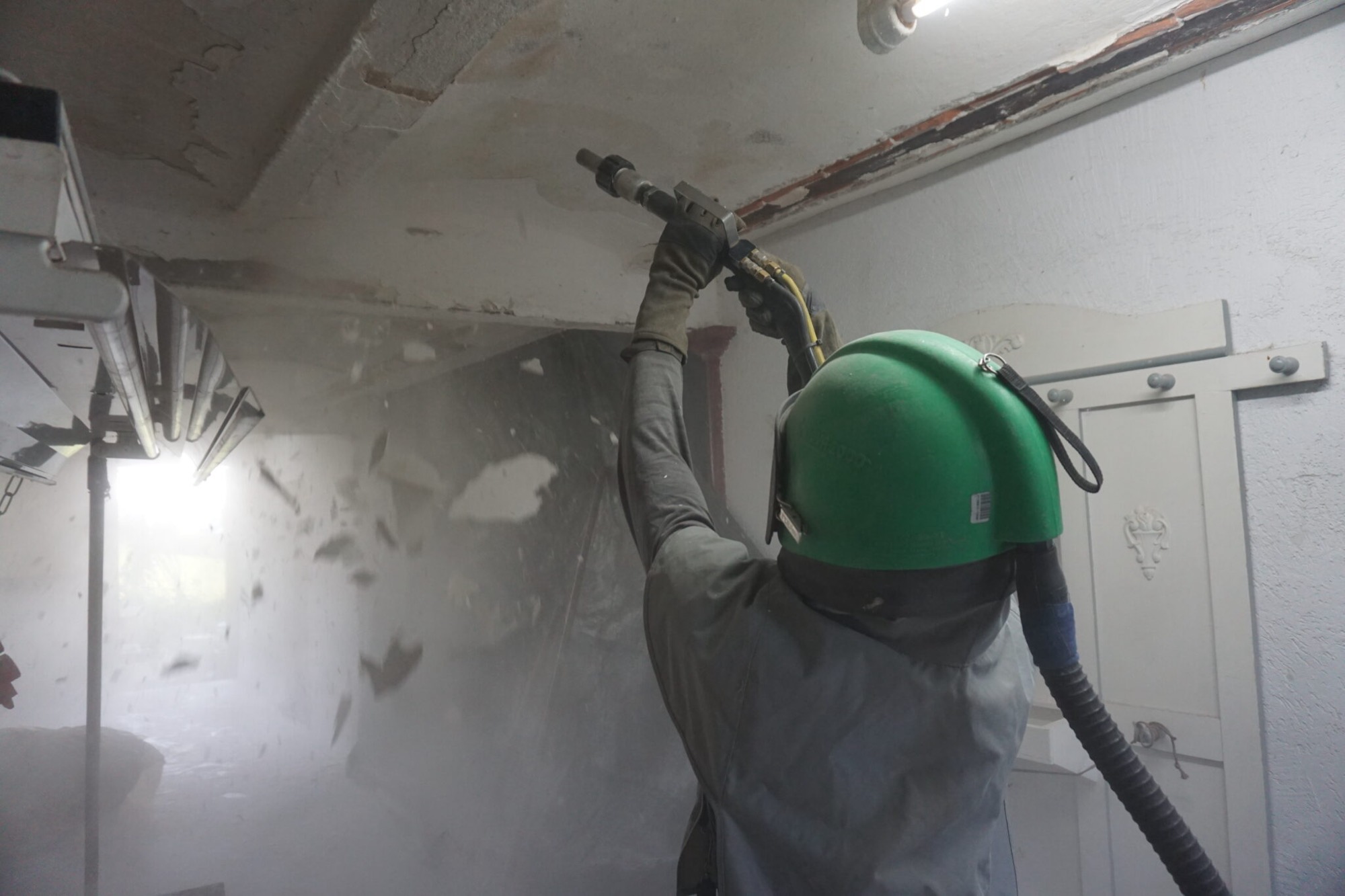 Operario de Sandblitz limpia con chorro de arena el techo de un edificio antiguo con equipo de protección
